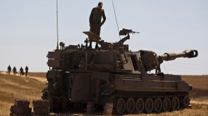 An Israeli soldier stands atop a mobile artillery unit stationed near the border with the Gaza Strip