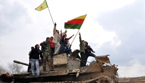 Civilians and members of the YPG gesture and raise flags atop a tank that belonged to fighters from the ISIL, in al-Manajeer village of Ras al-Ain countryside