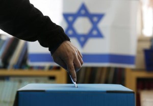 An Israeli flag is seen in the background as a man casts his ballot at a polling in a West Bank Jewish settlement, north of Ramallah