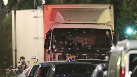 A policeman stands, watching the truck used for the attack near the scene of an attack after a truck drove onto the sidewalk late Thursday, and plowed through a crowd of revelers who gathered to watch the fireworks in the French resort city of Nice, southern France, Friday, July 15, 2016. (AP Photo/Luca Bruno)
