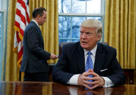 President Donald Trump sits at his desk as he waits for White House Chief of Staff Reince Priebus, left, to deliver three executive orders for his signature, Monday, Jan. 23, 2017, in the Oval Office of the White House in Washington. (AP Photo/Evan Vucci)