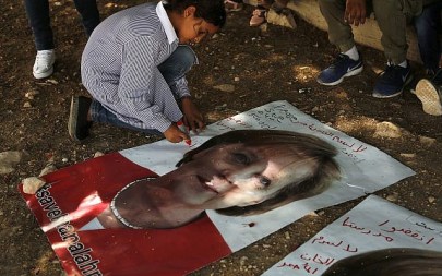 A Bedouin child writes on a picture of German Chancellor Angela Merkel ahead of her expected visit to Israel on Wednesday, in the West Bank Bedouin community of Khan al-Ahmar, Oct. 2, 2018. Arabic on the poster reads, "save Khan al-Ahmar" and "save our school." (AP Photo/Nasser Shiyoukhi)