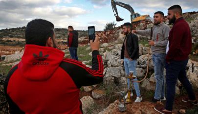 Lebanese villagers smoke a water pipe and take souvenir pictures in front of Israeli excavators, Mays al-Jabal, southern Lebanon, December 13, 2018.