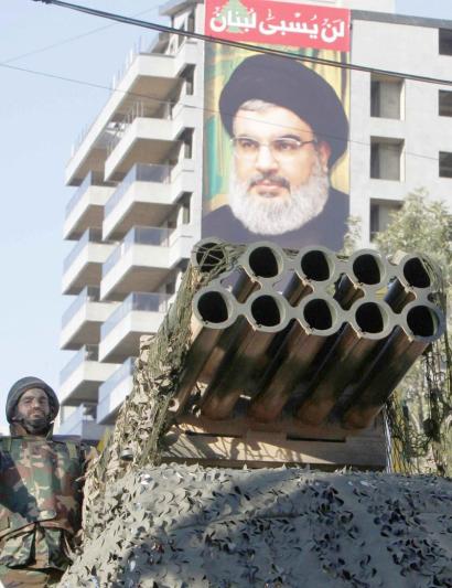 A Shia Hezbollah supporter stands on a rocket launcher in Nabatieh with a poster of Hezbollah leader Sayyed Hassan Nasrallah in the background. (Reuters)