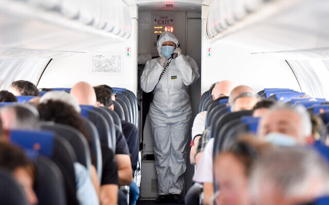 Illusrative: An Israir flight attendant wearing full protective gear walks next to passengers during an Israir flight between Tel Aviv and Eilat, May 13, 2020. (Yossi Zeliger/Flash90)