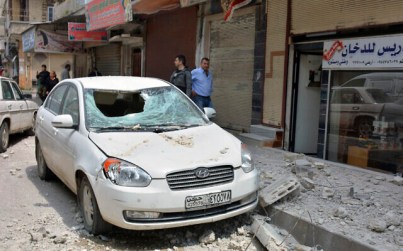 Illustrative: People stand near a car that was damaged due to flying debris from a Syrian military base housing a weapons warehouse, in the country's central province of Homs, Syria, May 1, 2020. (SANA, the Syrian official news agency, via AP)