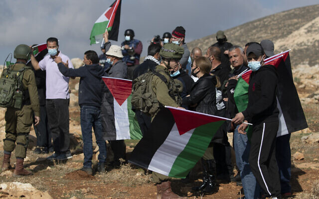 Israeli soldiers stop Palestinian protesters from reaching a Jewish settler outpost, at the outskirts of the West Bank village of Mughayer, north of Ramallah on December 18, 2020. (AP/Nasser Nasser)
