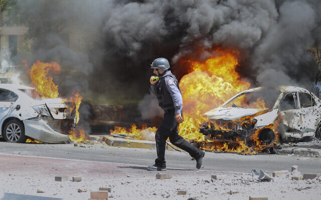 An Israeli firefighter walks next to cars hit by a rocket fired from Gaza Strip, in the southern Israeli town of Ashkelon, May 11, 2021. (AP Photo/Ariel Schalit)