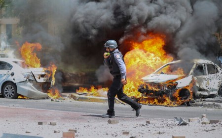 An Israeli firefighter walks next to cars hit by a rocket fired from Gaza Strip, in the southern Israeli town of Ashkelon, May 11, 2021. (AP Photo/Ariel Schalit)