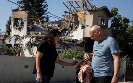A young girl is comforted by her father next to a house damaged by a rocket fired from the Gaza Strip, in Yehod, central Israel, May 12, 2021 (AP Photo/Heidi Levine)