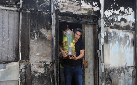 Man carries a Torah scroll from a torched synagogue in the central Israeli city of Lod, following a night of heavy rioting on May 12, 2021 (Yonatan Sindel/Flash90)